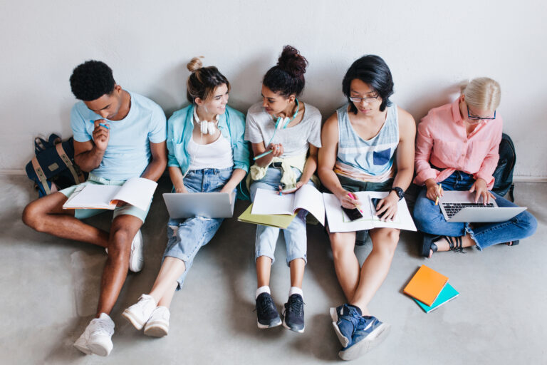 Overhead portrait of international students waiting for test in college. Group of university mates sitting on the floor with books and laptops, doing homework..